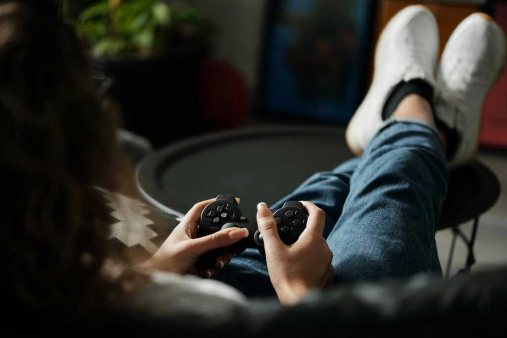 Close-up of woman gaming with a controller, feet propped up, enjoying leisure time indoors.